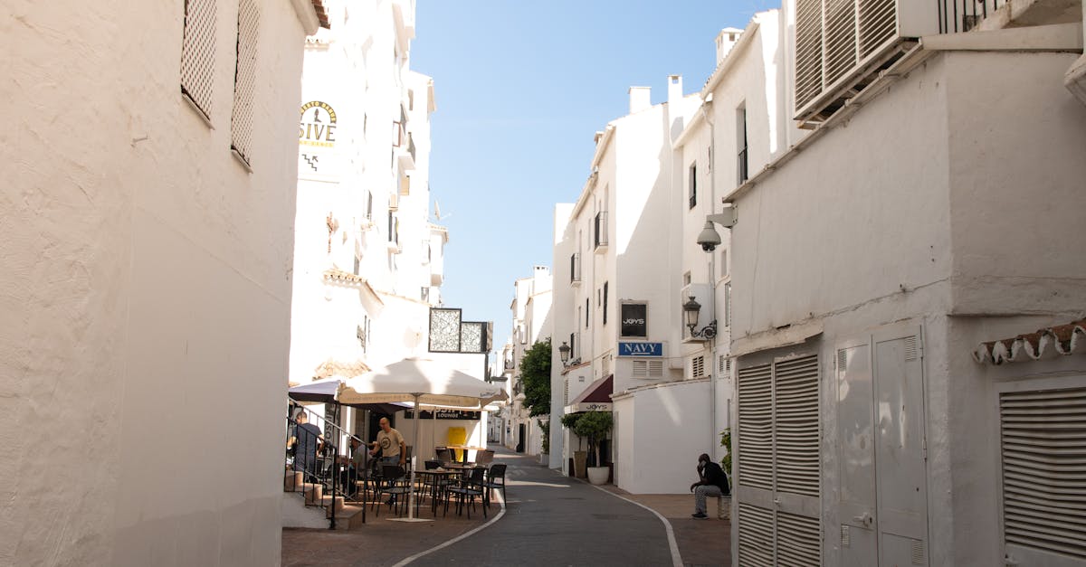 A serene whitewashed alley in Spain with outdoor dining on a sunny day.