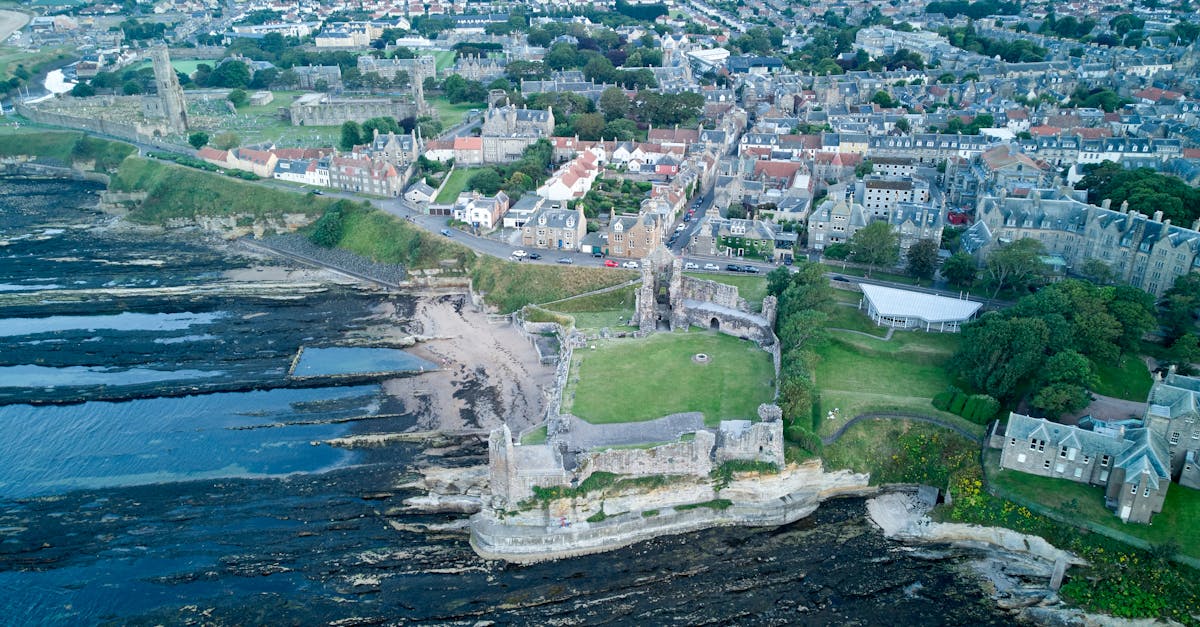 Drone shot of St Andrews Castle and coastal city in Fife, Scotland, showcasing historical architecture and scenic seashore.