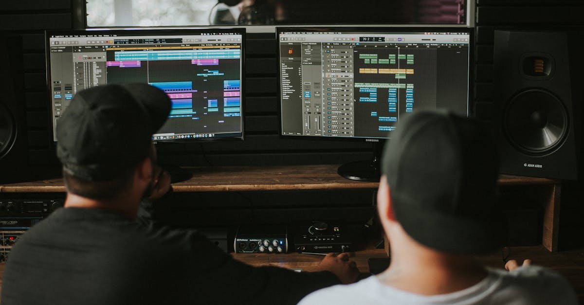 Two men working in a music studio with dual monitors displaying audio editing software.