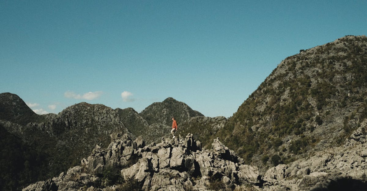 A lone hiker explores a rugged mountain landscape under a clear blue sky, embodying the spirit of adventure.