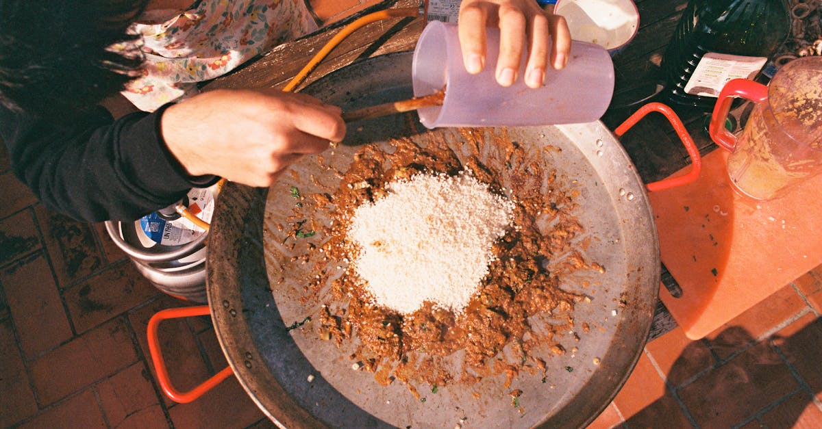 Overhead view of a person preparing a dish with grains and spices, adding liquid.