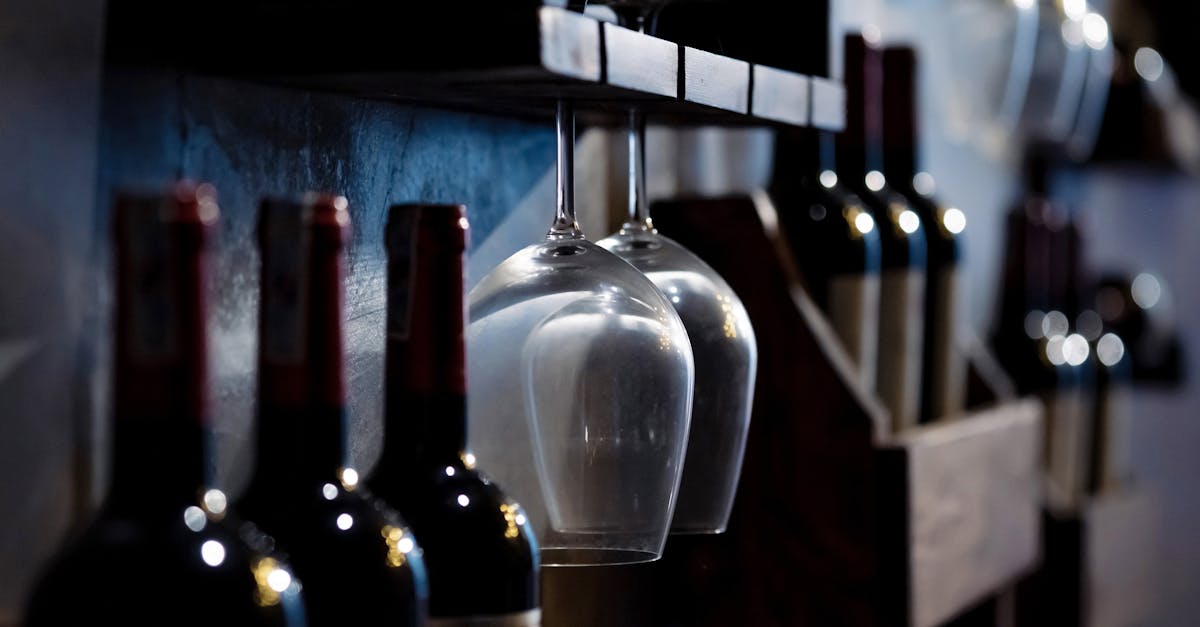 Close-up of wine bottles and glasses on wooden shelves in a dimly lit cellar, creating a cozy ambiance.