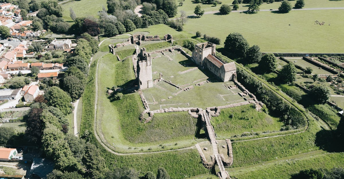 An aerial view of ancient castle ruins surrounded by verdant countryside and nearby village.