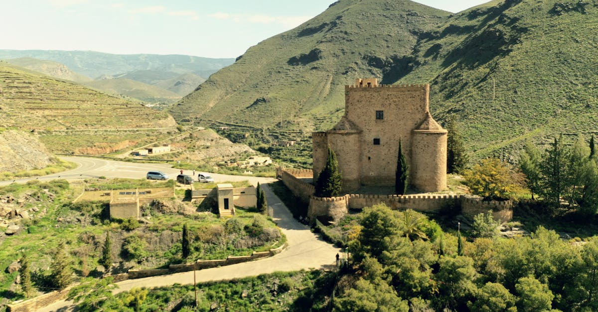 Drone shot of a historic castle surrounded by lush hills in a green valley.