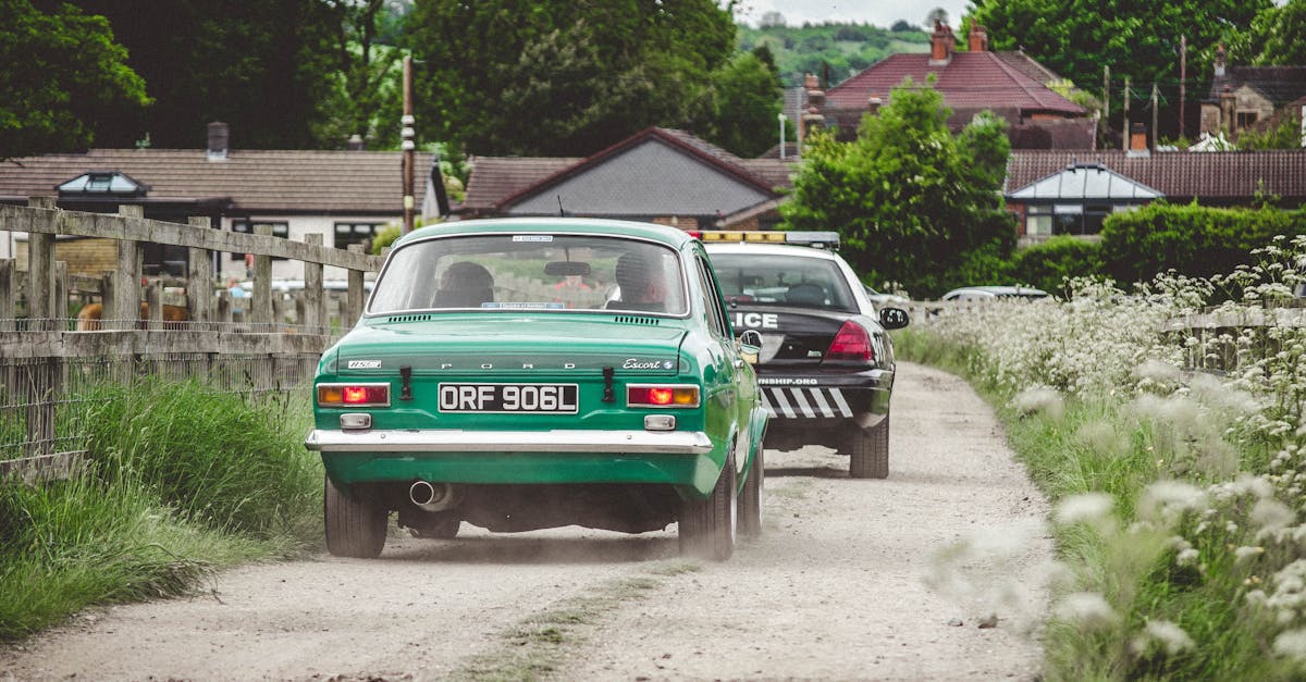 Vintage car being chased by police on a dirt road in a countryside town.