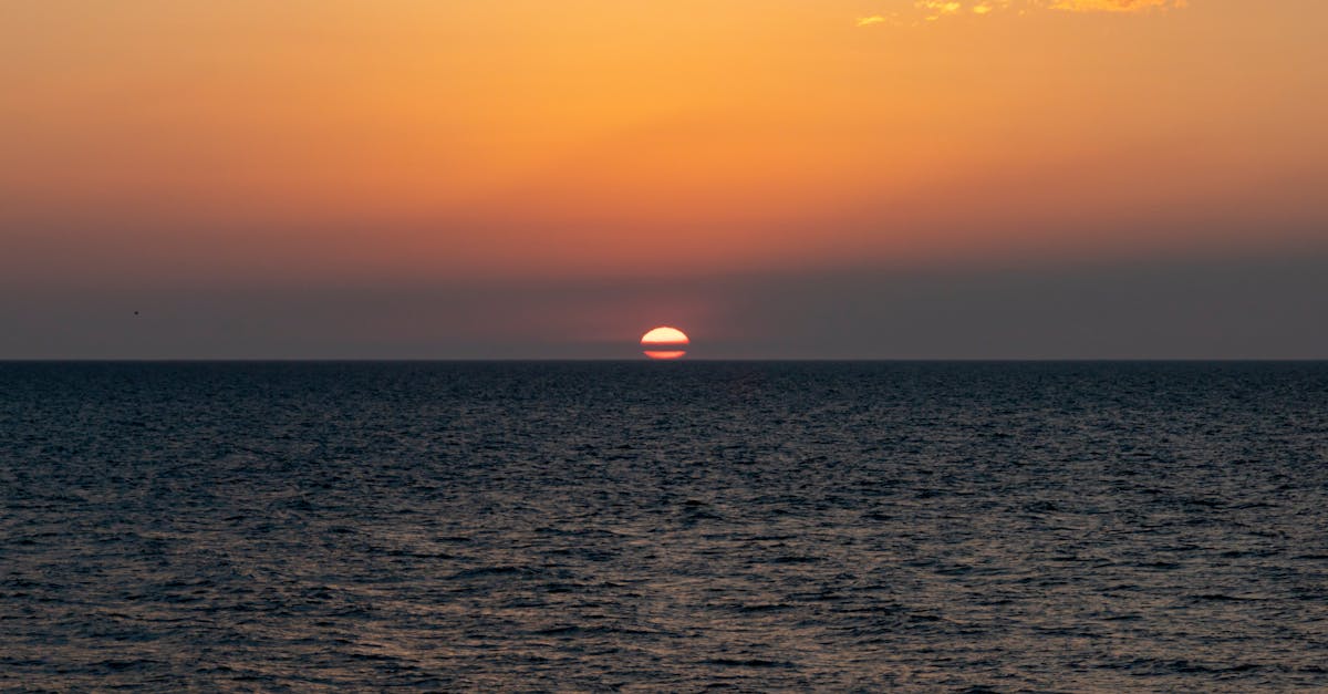 Breathtaking view of the sun setting over the ocean, creating a vivid orange sky and serene water reflection.
