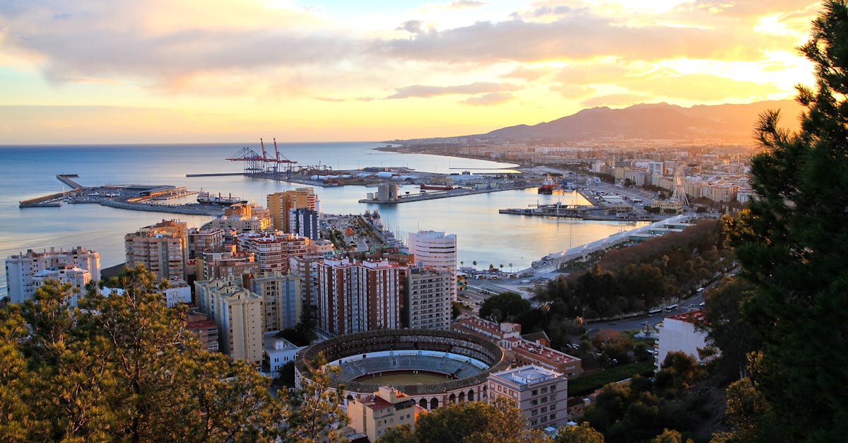 Captivating aerial view of Málaga at sunset, showcasing the port and iconic bullring, with mountains in the background.