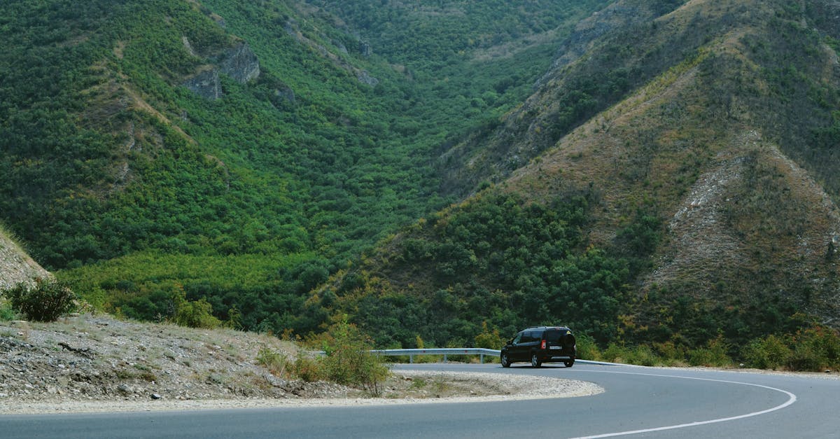 A black car navigating a winding road through lush green mountains, perfect for travel themes.