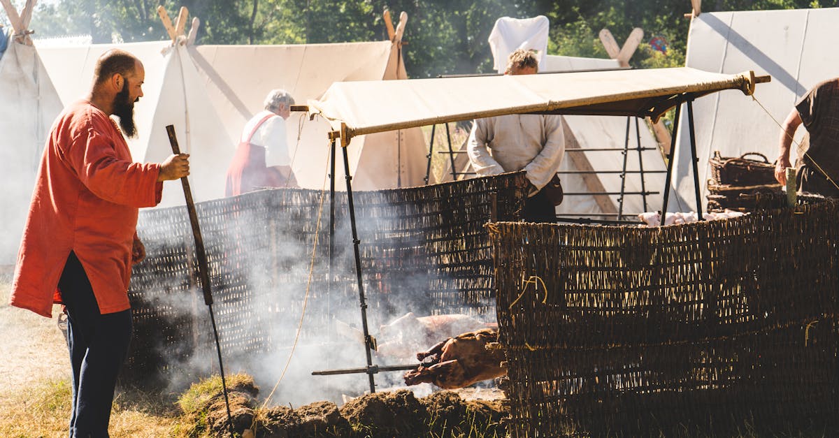 A man in traditional attire cooks over an open flame at a historical reenactment camp.