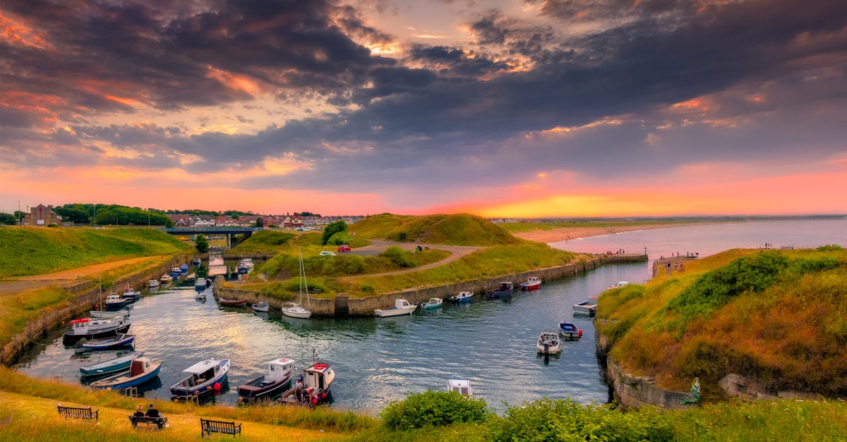 Stunning sunset over Seaton Sluice harbor with moored boats and vibrant landscape.