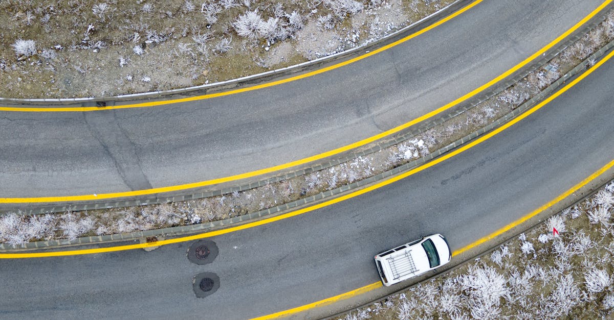 Drone shot capturing a winding road and a white car amidst frosty landscape in Ankara.