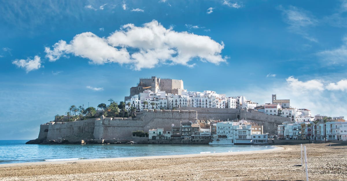 Picturesque coastal town with historic castle and sandy beach under blue skies.