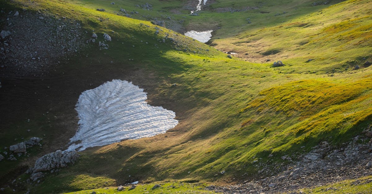 Beautiful alpine landscape with green hills and remaining snow patches, bathed in sunlight.