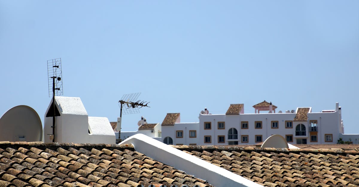 Aerial view of traditional tiled rooftops and antennas with white buildings in the background under a clear blue sky.