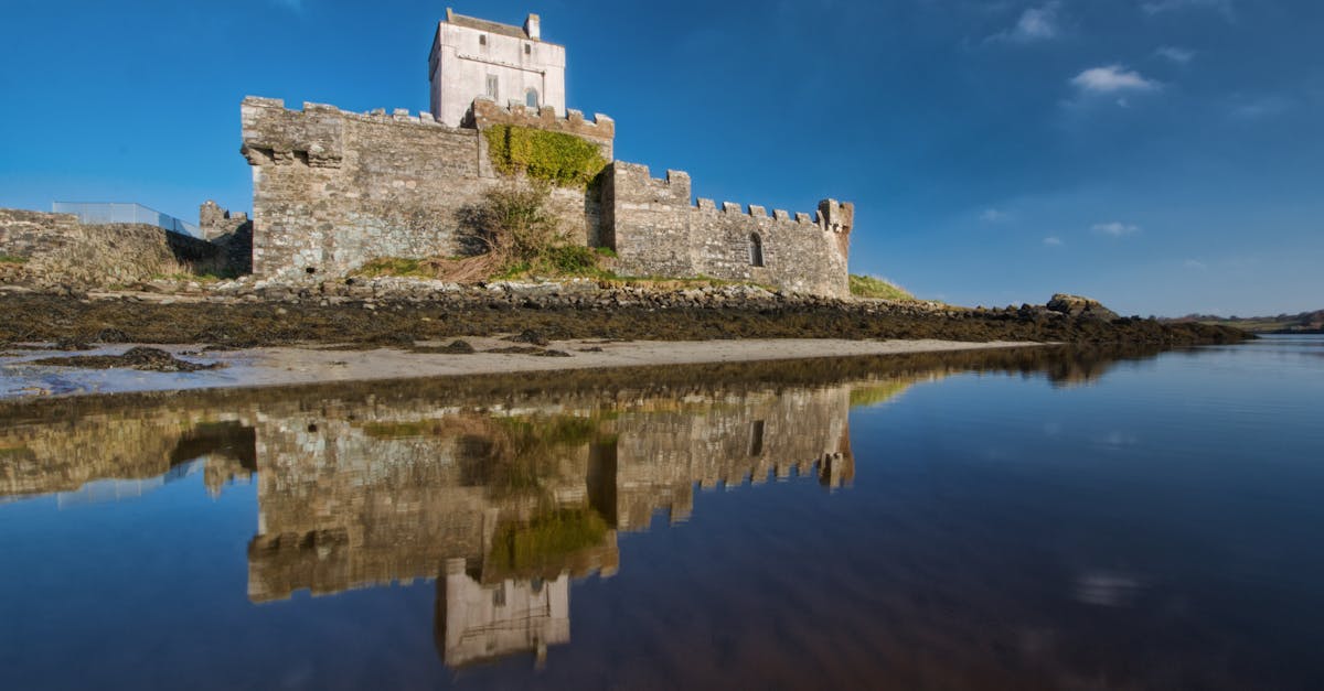 A stunning view of Doe Castle in County Donegal, Ireland reflecting in calm waters under a clear blue sky.