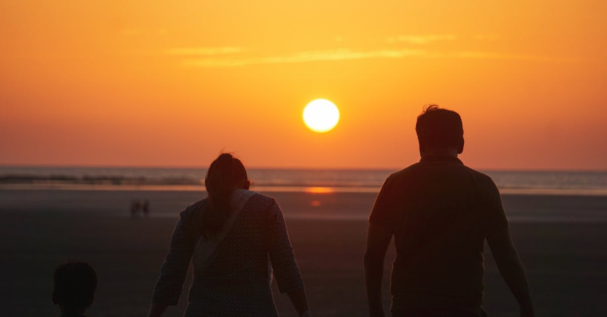 A family enjoys a serene sunset walk along the beach, captured in silhouette.