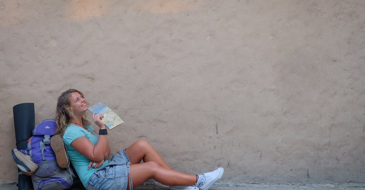 Smiling female traveler sitting by a wall with a map, enjoying a moment of relaxation on her journey.