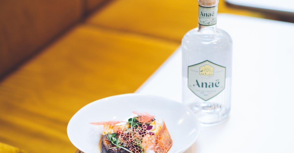 A gourmet dish served alongside a bottle of Anaé gin on a clean and modern setup.