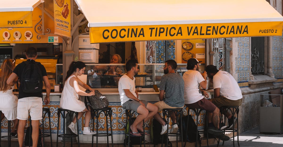 People enjoying food at a Valencian street stall under a bright yellow awning.