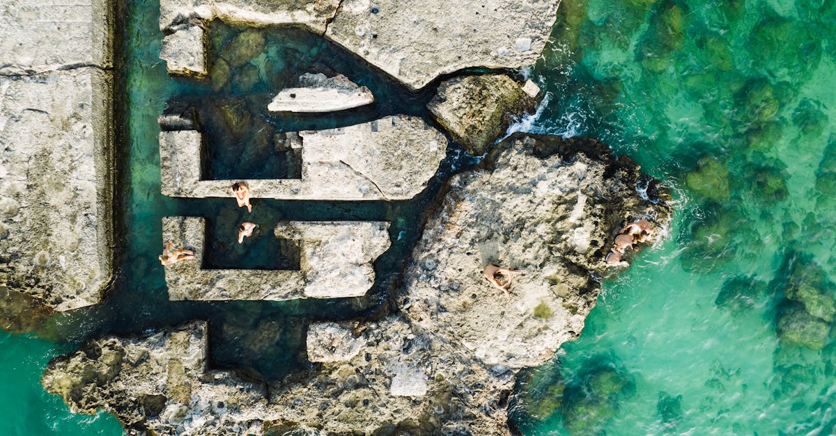 Breathtaking aerial shot of Monopoli's rocky coastline with swimmers enjoying the turquoise sea.
