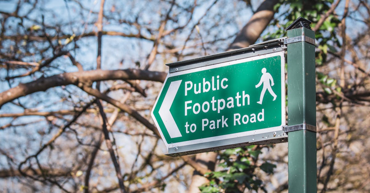 Green public footpath sign in a Bristol park, guiding pedestrians with trees in the background.