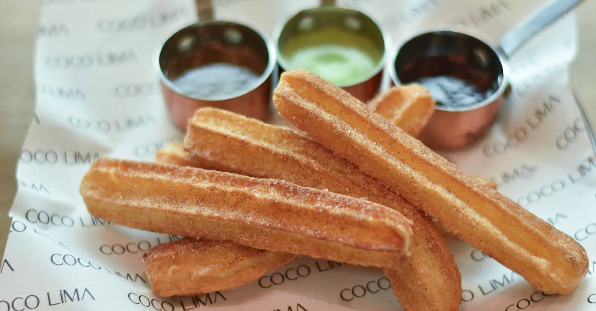 Close-up of crispy churros with dipping sauces on branded paper, perfect sweet dessert.