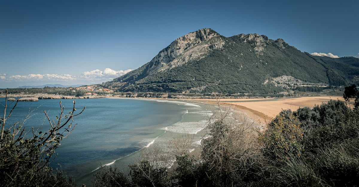 Beautiful coastal view of beach and mountainous landscape in Castro-Urdiales, Spain, under a clear blue sky.
