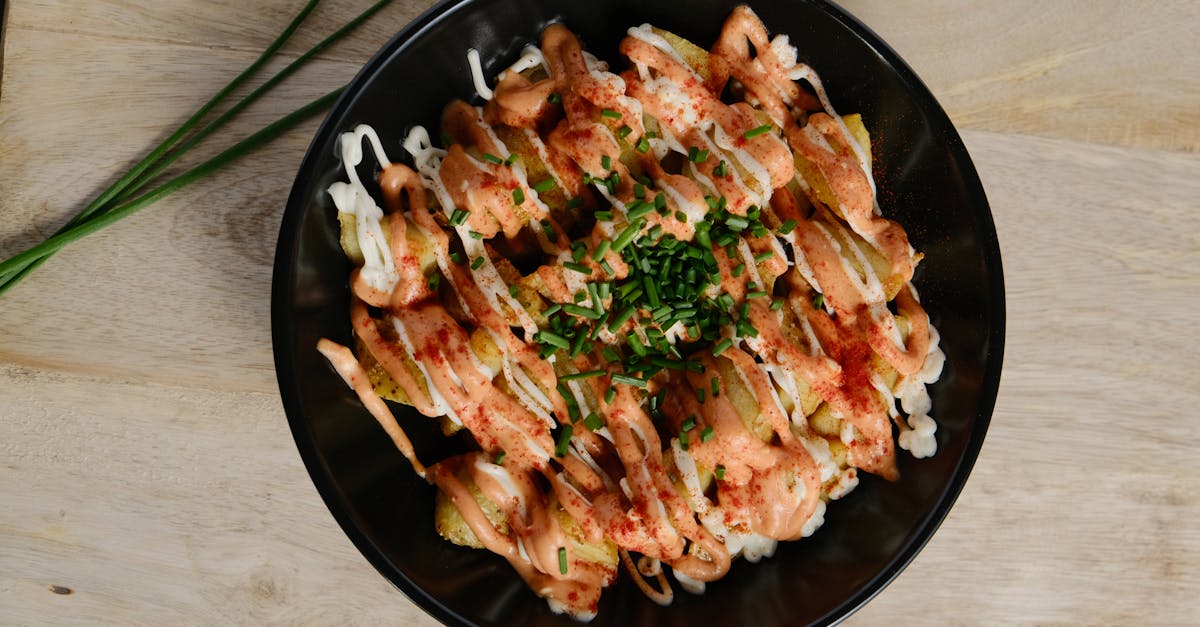 Delicious gourmet fries topped with spicy sauce and fresh chives in a black bowl.