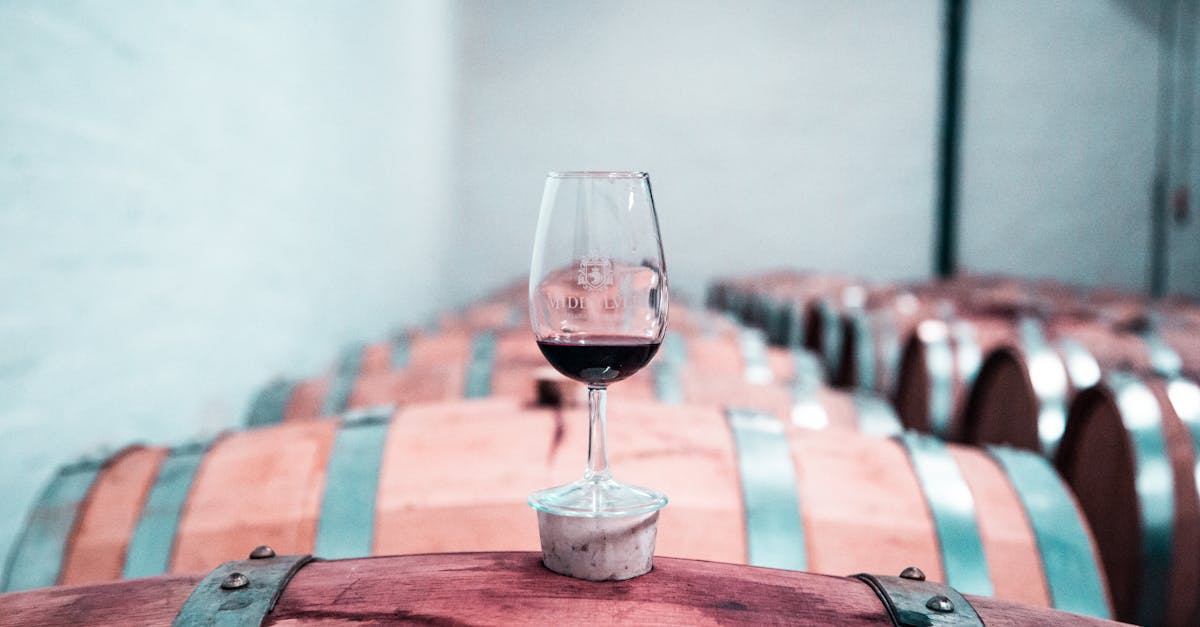 A glass of red wine sits elegantly on an oak barrel in a Stellenbosch winery cellar.