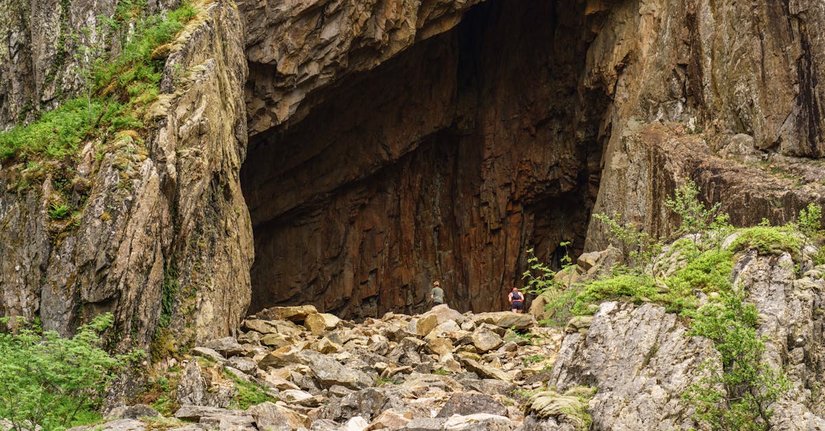 Explore the grand entrance of a cave in Brønnøysund, Norway, amidst rugged rocks and lush greenery.