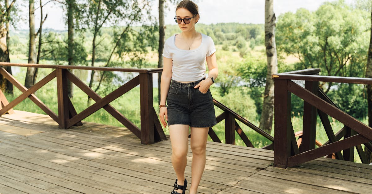 Woman in casual summer attire walks on a wooden deck amid lush green park.