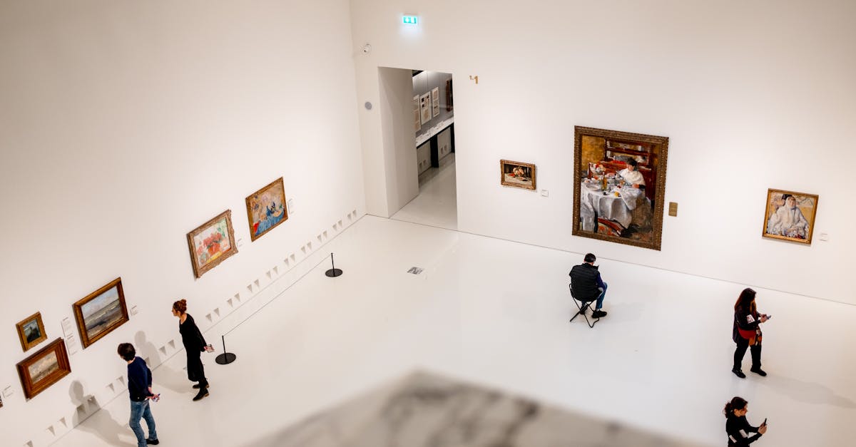 Visitors exploring an art gallery with various paintings on display from a high angle view.