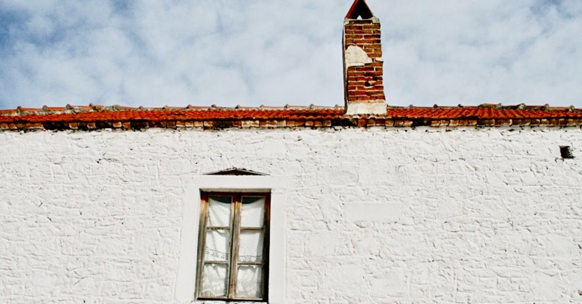 A historic whitewashed building with a red brick chimney set against a blue sky.