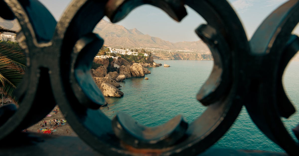 Ocean view framed by artistic ironwork railing with distant cliffs and mountains.
