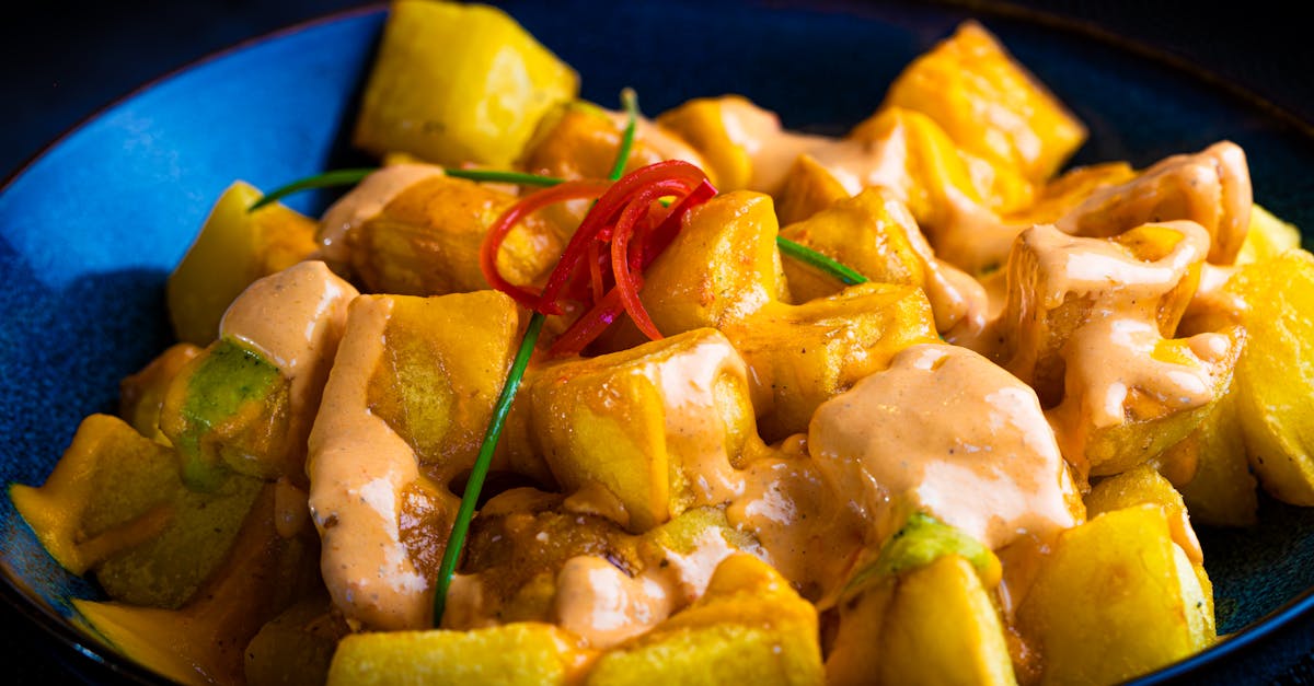 Close-up of patatas bravas with spicy aioli in a vibrant blue bowl.