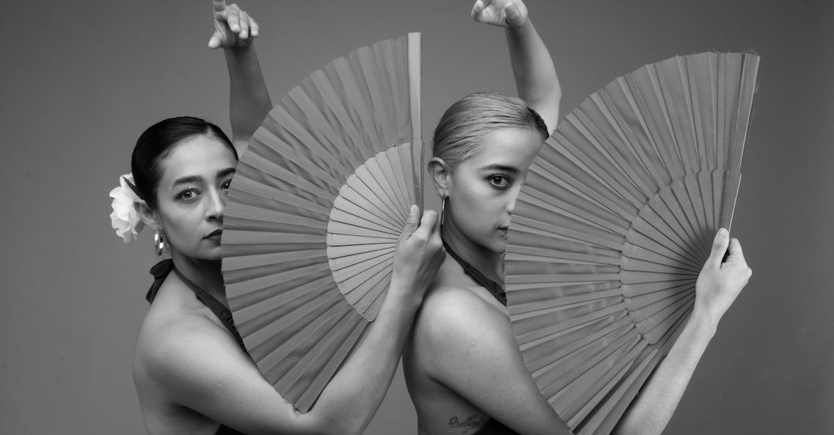 Black and white photo of two female flamenco dancers gracefully posing with fans, capturing Spanish cultural essence.