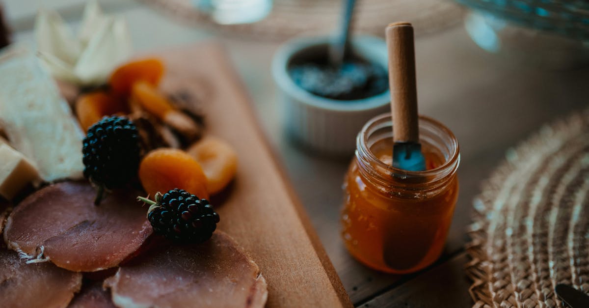 A rich charcuterie board featuring meats, cheese, and fruits with a jar of honey.