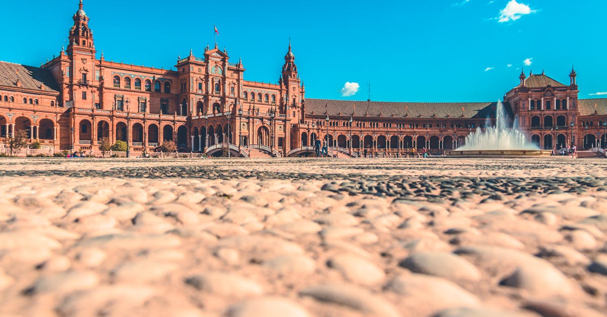 A scenic view of Plaza de España in Seville, Spain, featuring the iconic fountain and unique architecture under a clear blue sky.