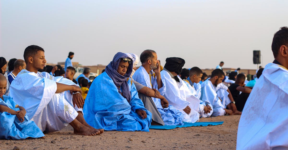 A group of people dressed in blue and white robes gathered for prayer in a desert landscape during daytime.