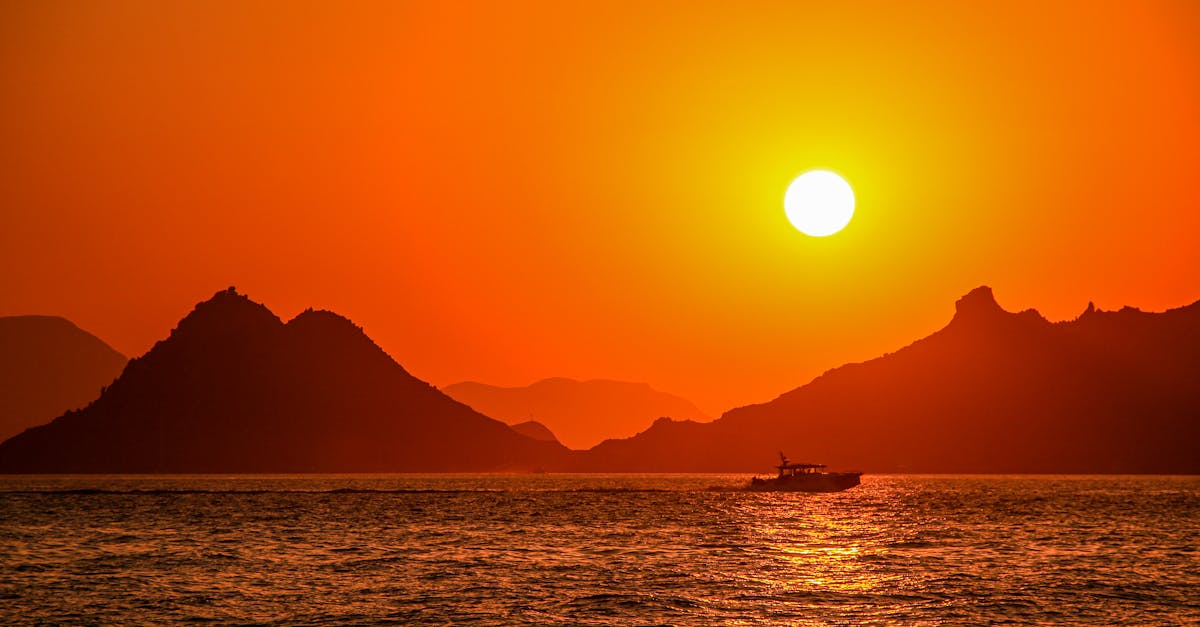 Silhouette of a boat sailing under a stunning sunset with mountains in the background.