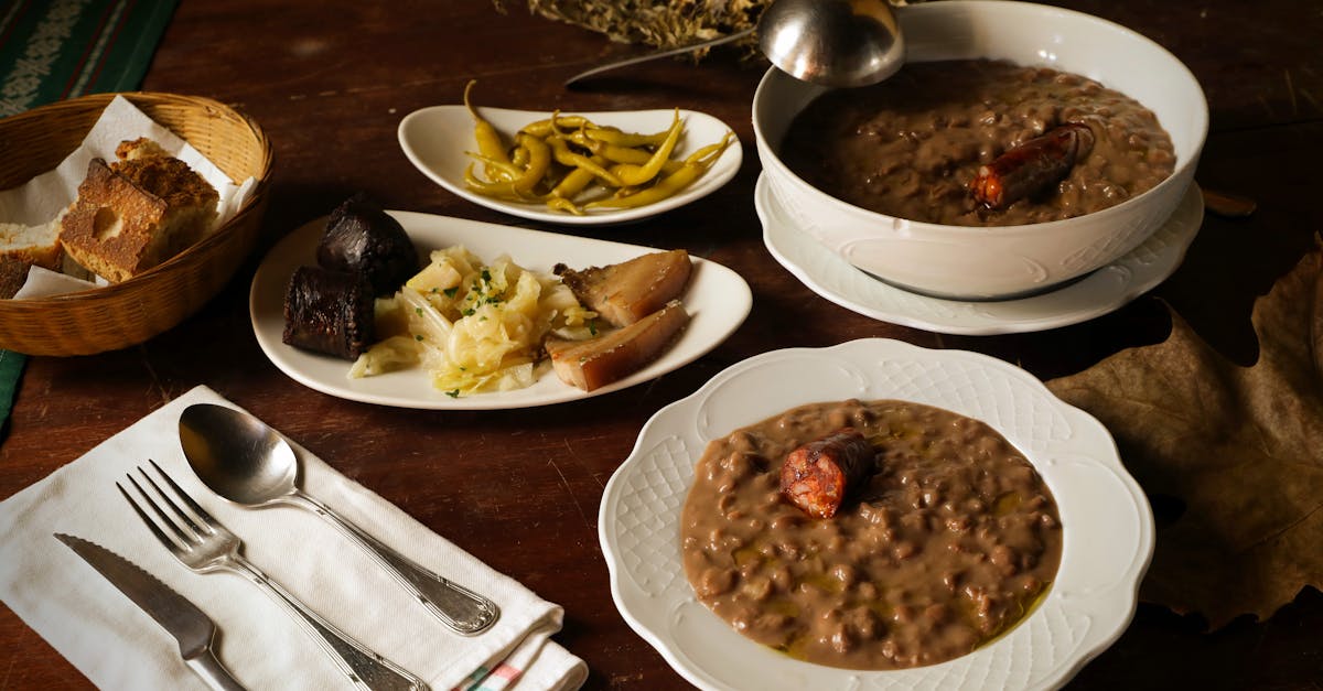 Rustic bean soup with sausages served with bread, peppers, and cabbage on a wooden table.