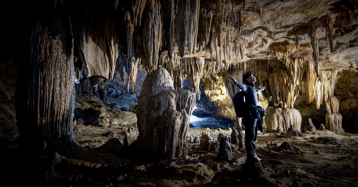 A man admires fascinating stalactites and stalagmites inside a vast cave, illuminated by subtle light.