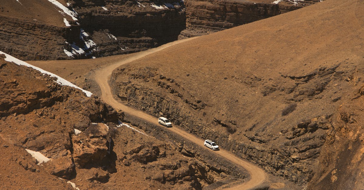 Two vehicles navigate a winding mountain road in the rugged Spiti Valley, Himachal Pradesh.