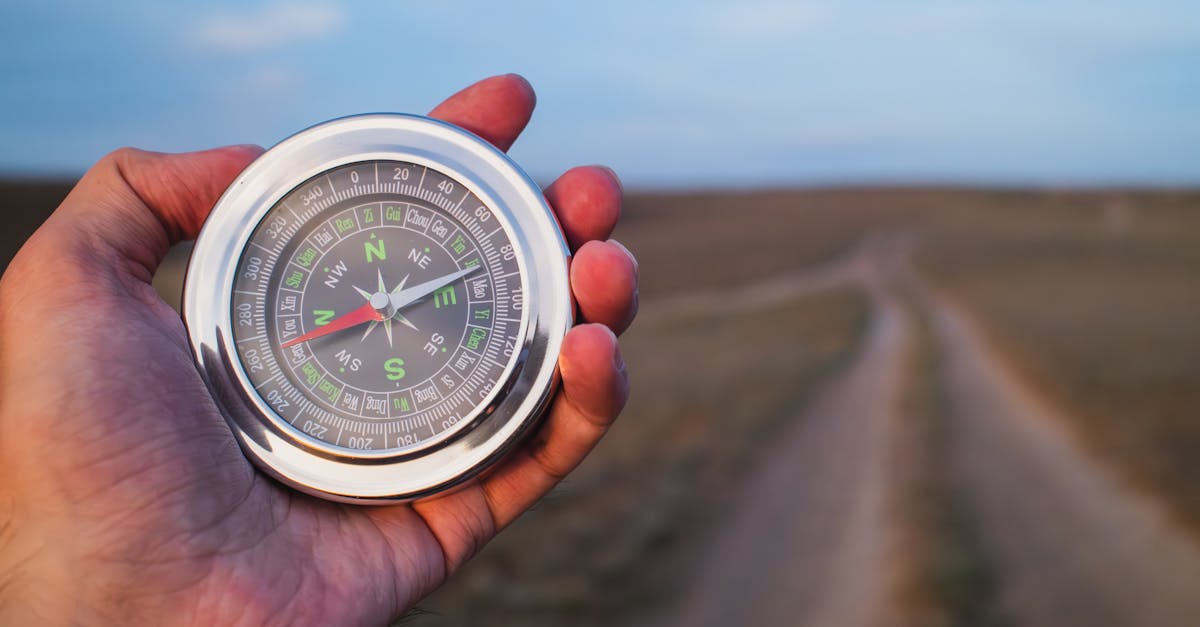 Close-up of a hand holding a compass against a rural path, symbolizing exploration.