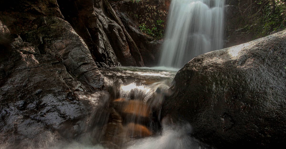 A tranquil waterfall flowing over smooth rocks surrounded by lush greenery in a serene forest setting.