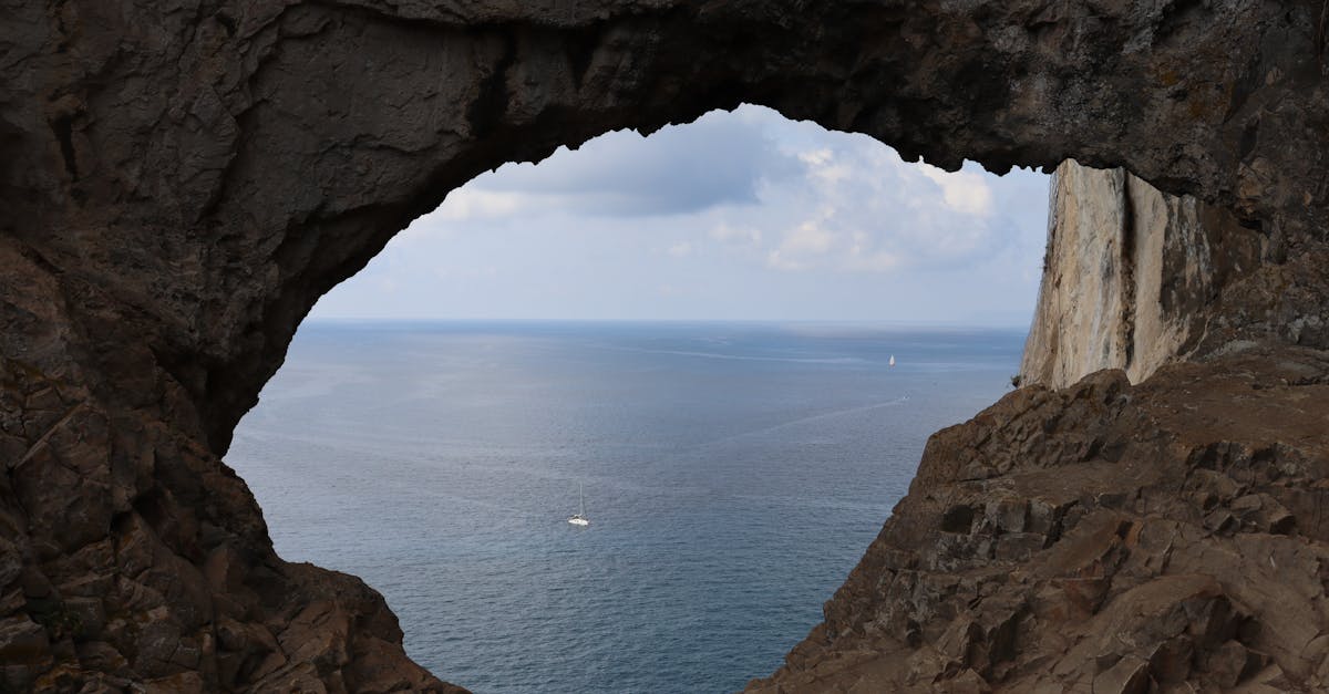 Dramatic rocky arch framing the clear Mediterranean Sea in Noli, Liguria, Italy.
