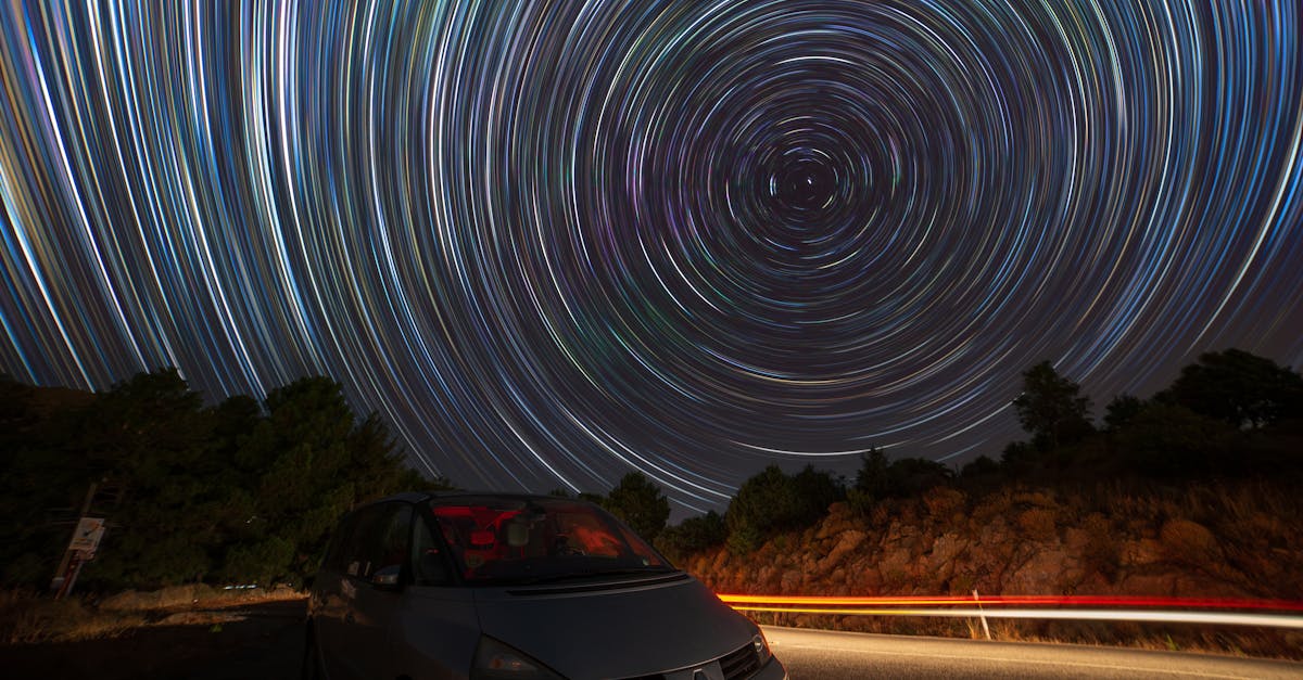 Stunning long exposure of star trails over a countryside road with parked car under the night sky.