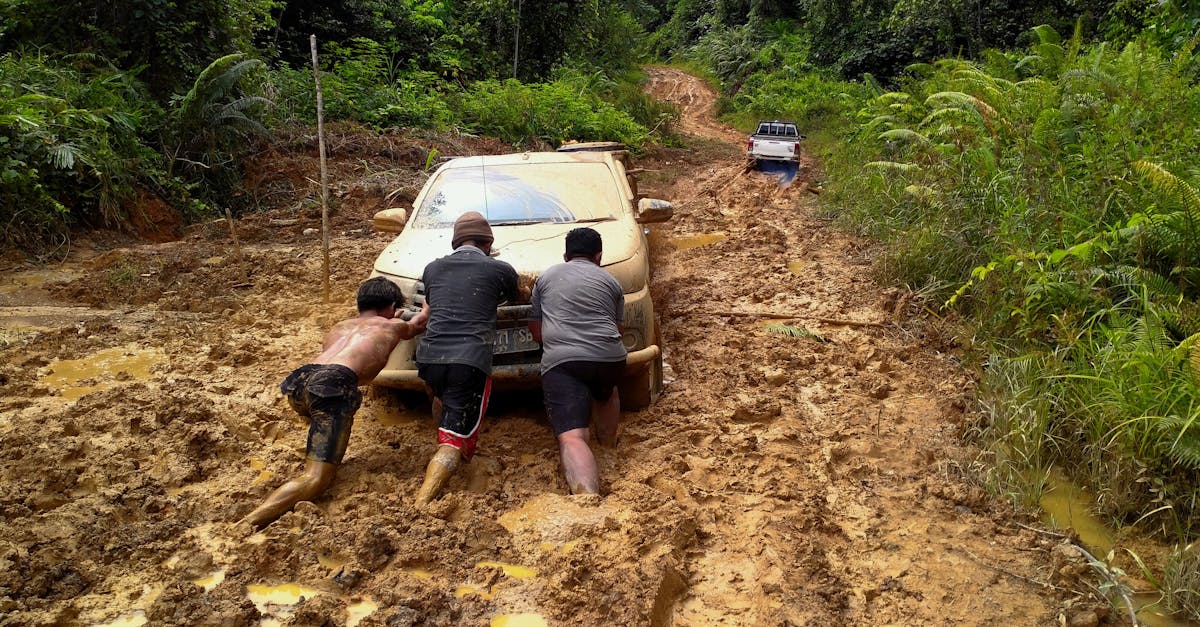 Three men push a car through a muddy forest road in North Kalimantan, Indonesia.