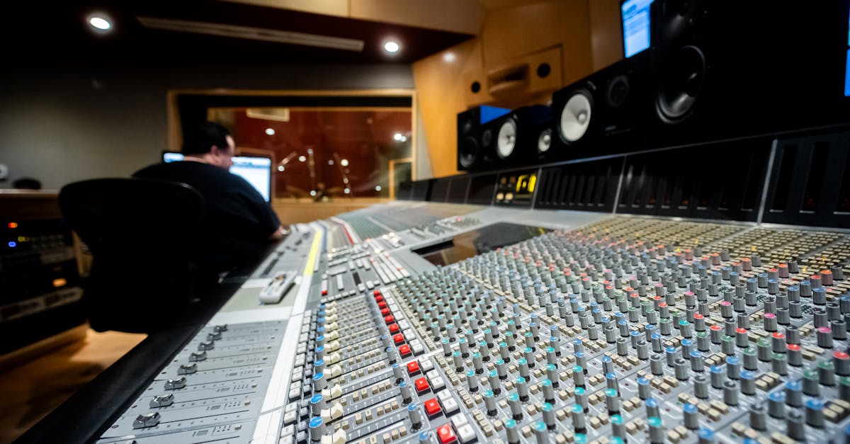 Close-up of a modern mixing console in a music recording studio with a sound engineer in the background.