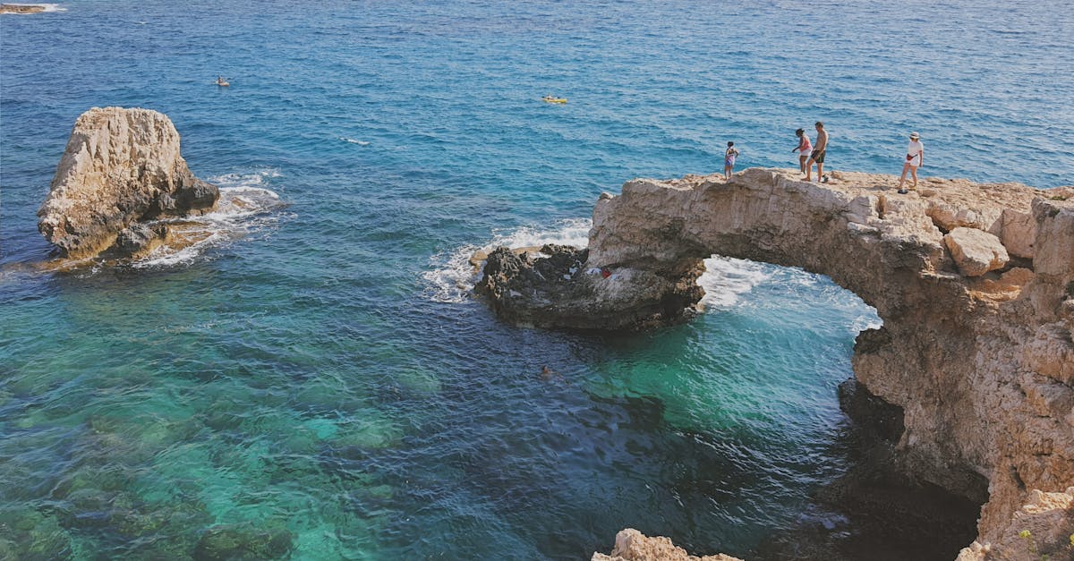 Tourists explore a natural rock arch over turquoise waters on a sunny day in Cyprus.